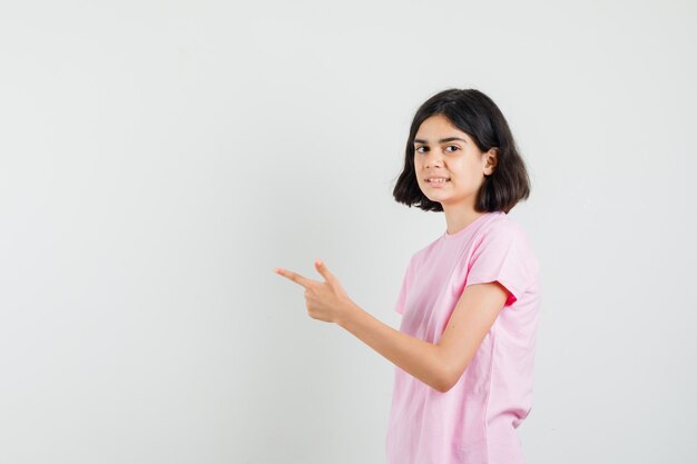 Little girl pointing away in pink t-shirt and looking cheery .