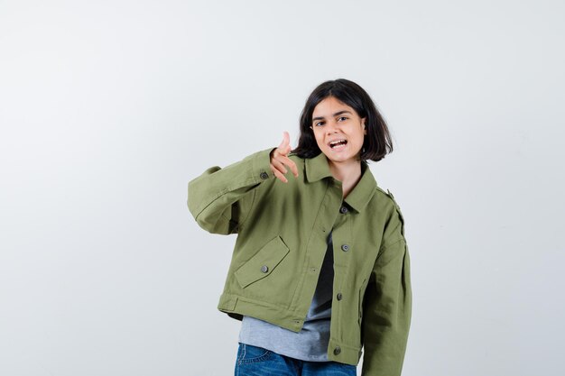 Little girl pointing in coat, t-shirt, jeans and looking positive , front view.