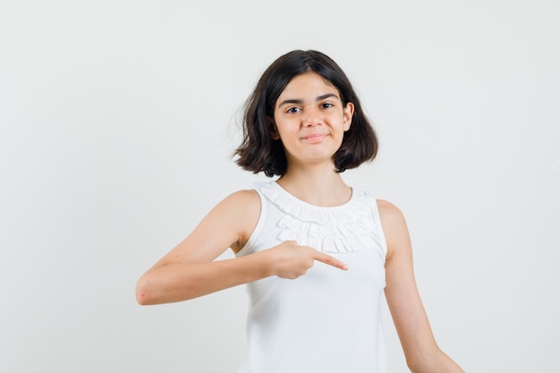 Little girl pointing down in white blouse and looking cheerful. front view.