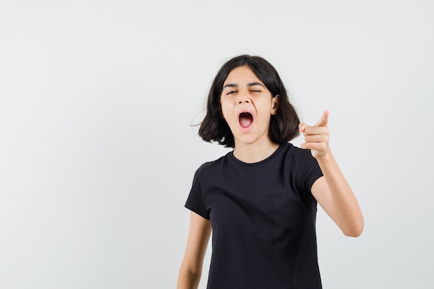 Little girl pointing at front while yawning in black t-shirt front view.