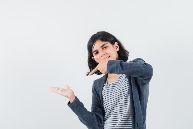 Little girl pointing at her empty palm in t-shirt, jacket and looking fatigued.