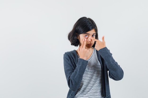 Tシャツ、ジャケットで指で引っ張られたまぶたを指している少女