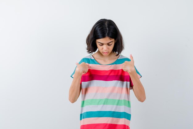 Little girl pointing at herself in t-shirt, jeans and looking serious. front view.