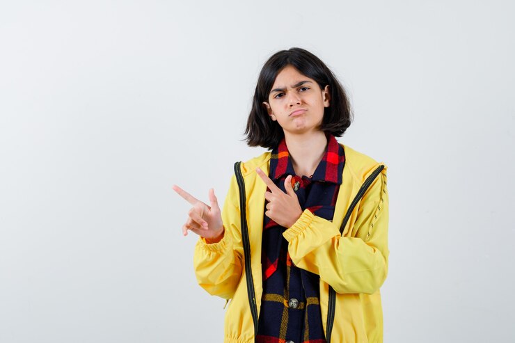 मुफ़्त फोटो little girl pointing to the left side in checked shirt, jacket and looking confident 