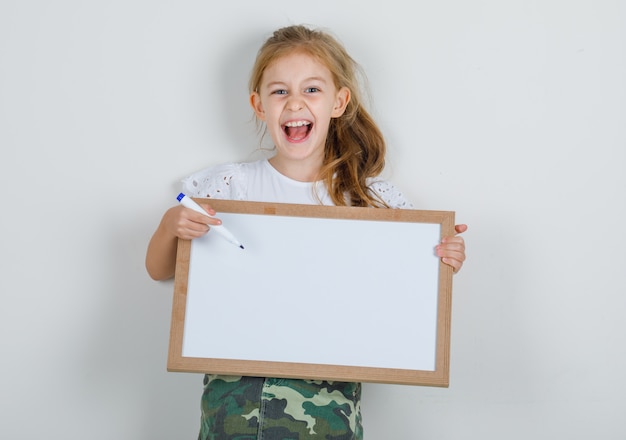 Маленькая девочка, указывая ручкой маркера на белую доску в белой футболке