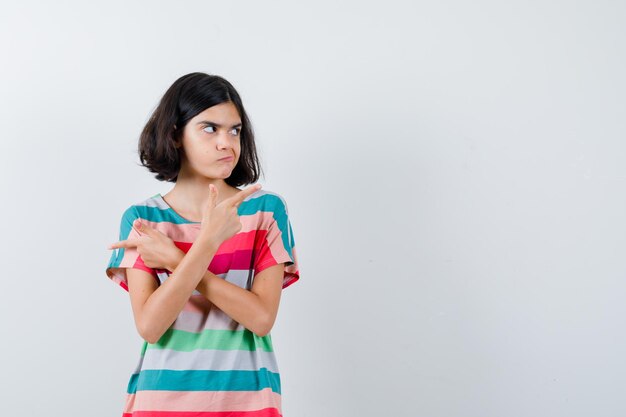 Little girl pointing opposite directions in t-shirt, jeans and looking serious , front view.