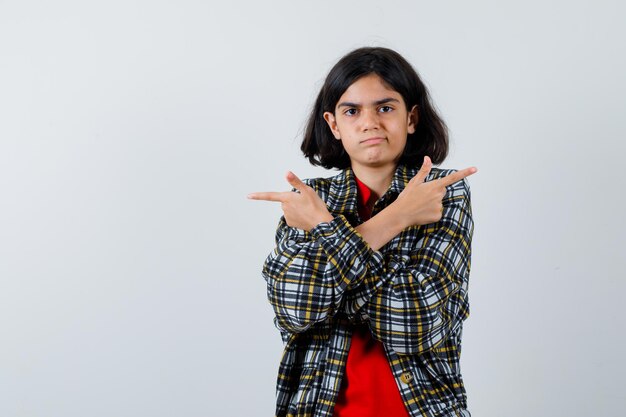 Little girl pointing at reverse sides with crossed hands in shirt,jacket and looking confused. front view.