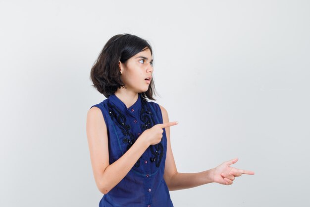 Little girl pointing to the right side in blue blouse and looking puzzled