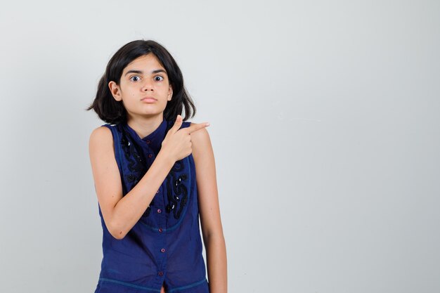 Little girl pointing to the side in blue blouse and looking puzzled