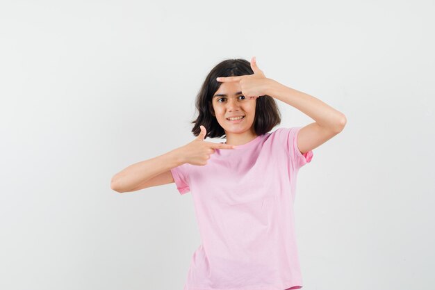 Little girl pointing to the side in pink t-shirt and looking merry. front view.