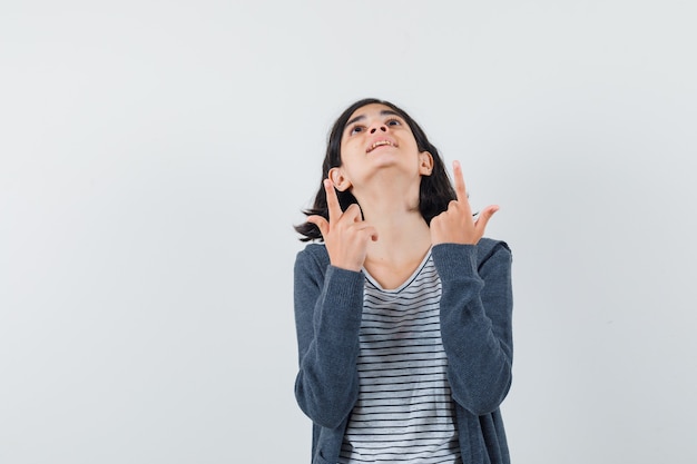 Little girl pointing up in t-shirt, jacket and looking happy