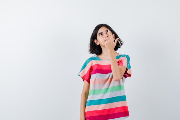Маленькая девочка указывая вверх в футболке и глядя с надеждой, вид спереди.