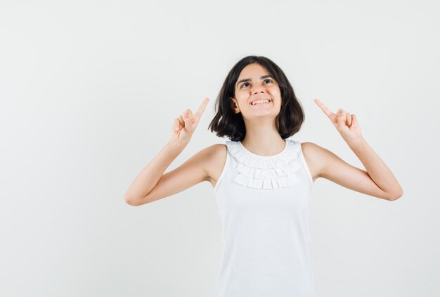 Little girl pointing up in white blouse and looking cheerful , front view.