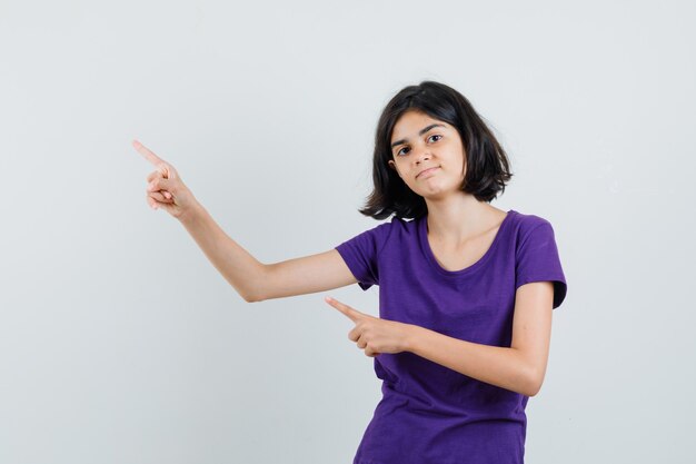 Little girl pointing at upper left corner in t-shirt and looking confident ,