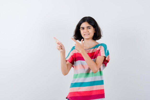 Little girl pointing upper left side in t-shirt  and looking happy. front view.