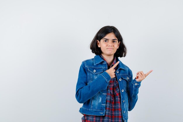 Little girl pointing at upper right corner in shirt, jacket and looking confident. front view.