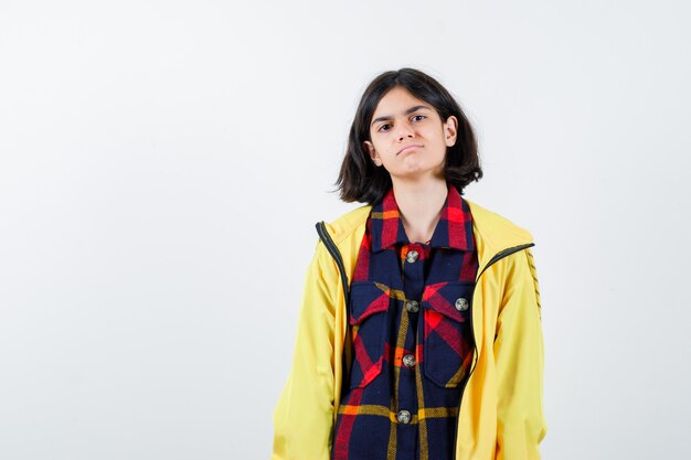 Little girl posing while standing in checked shirt, jacket and looking confident 