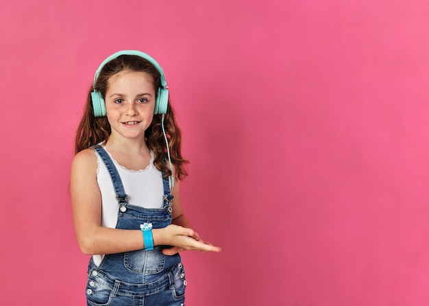 Little girl posing with headphones on a pink wall