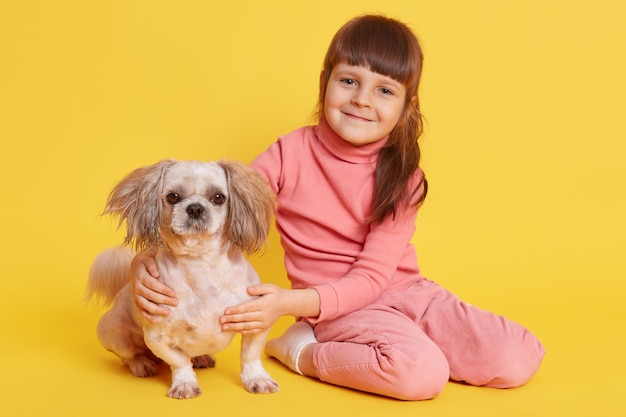Little girl posing with Pekingese dog on yellow
