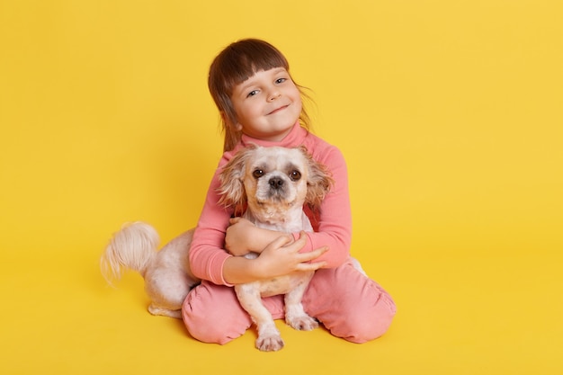 Free photo little girl posing with pekingese dog on yellow