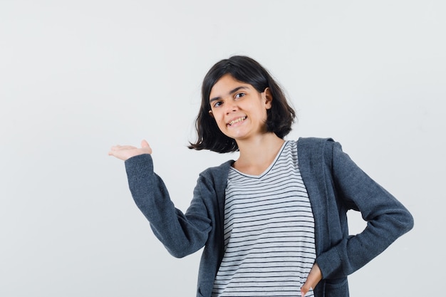 Little girl presenting something or welcoming in t-shirt, jacket and looking confident.