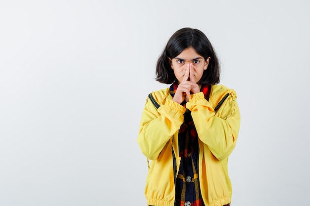 Little girl pressing nose with fingers in checked shirt, jacket and looking serious 