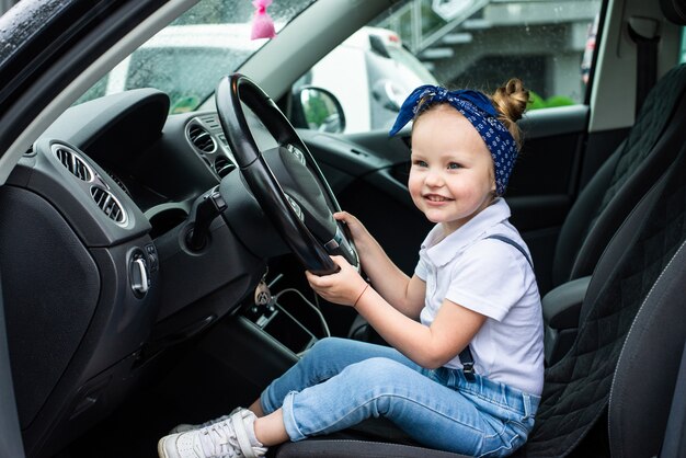 小さな女の子が車を運転するふりをします。子供の教育、学習、車の運転、面白い、幸せ、遊び、幸福、自動車保険の概念