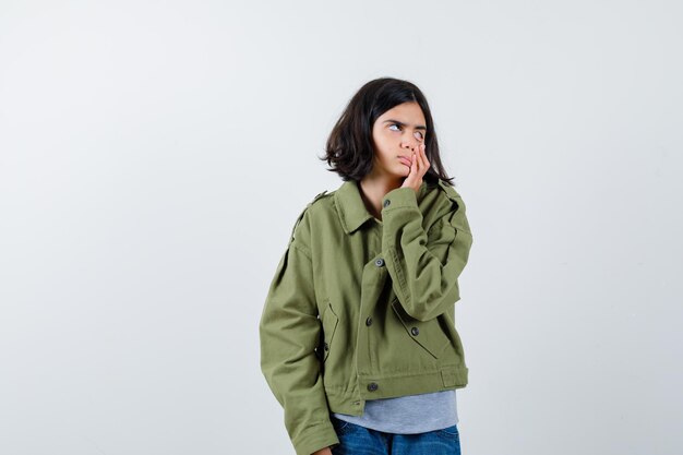 Little girl pulling down eyelid with finger in coat, t-shirt, jeans and looking tired. front view.