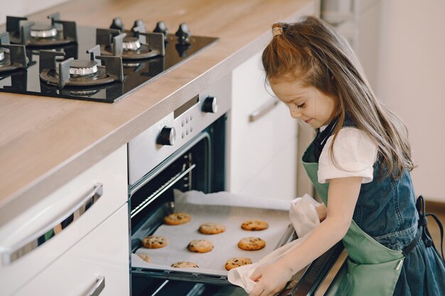 小さな女の子がオーブンからクッキートレイを引っ張る