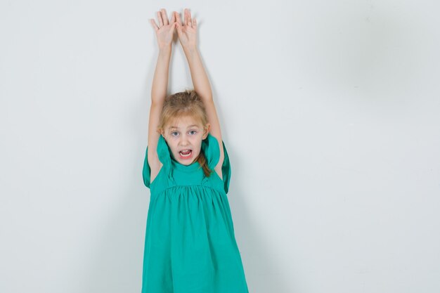 Маленькая девочка поднимает руки с открытым ртом в зеленом платье