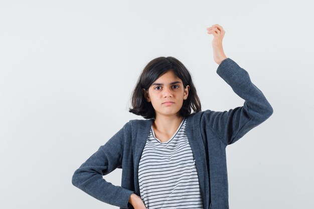 Little girl raising hand in t-shirt, jacket and looking confused