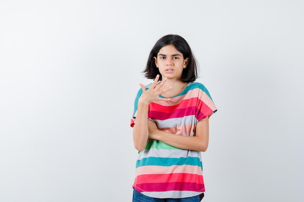 Маленькая девочка поднимает руку, пожимая плечами в футболке и озадаченная, вид спереди.