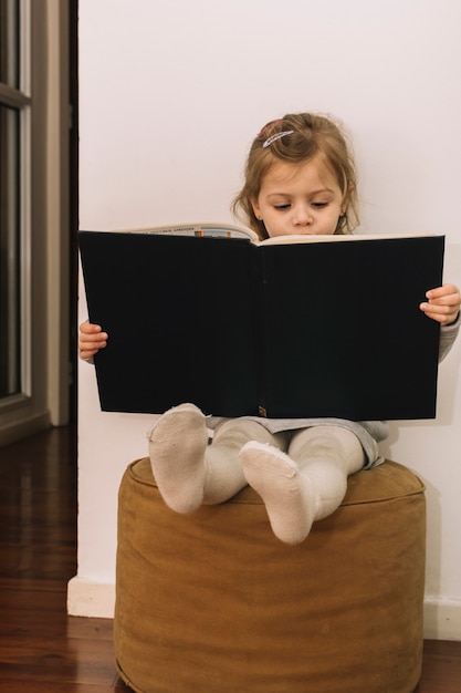 Little girl reading book on pouf