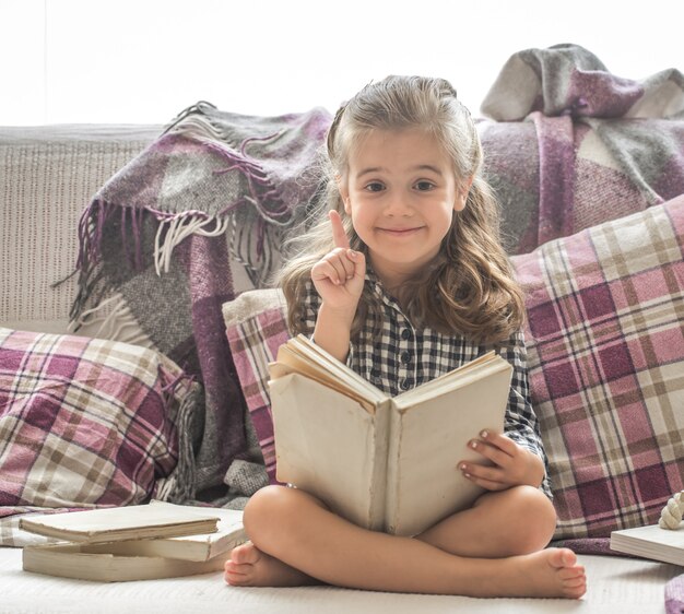 маленькая девочка читает книгу на диване