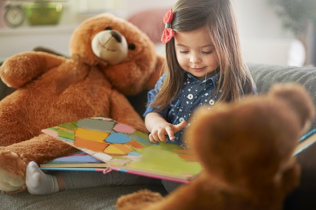 Little girl reading a book with her teddy bears