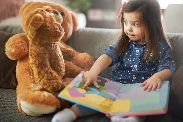 Little girl reading a book with her teddy bears