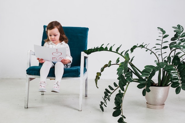 Little girl reading greeting card with I love mom inscription 