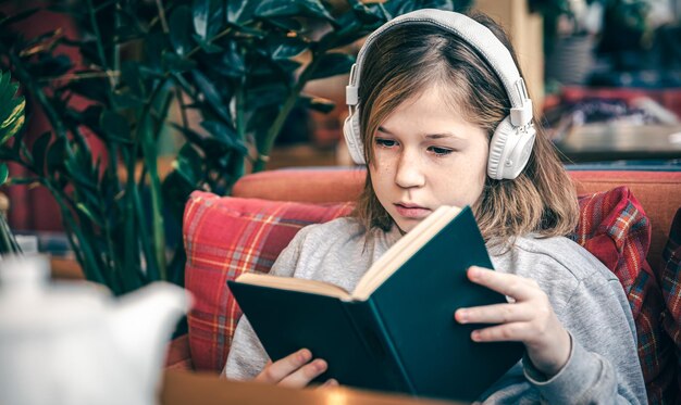 A little girl reads a book and listens to music on headphones