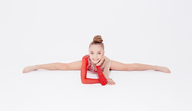 Little girl in red dress doing gymnastic split. Isolated on white background.