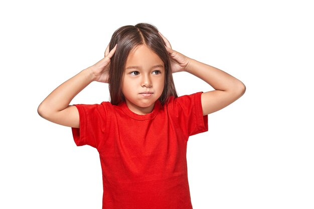 Little girl in red t-shirt closed her ears with hands and does not want to listen anyone isolated on white background