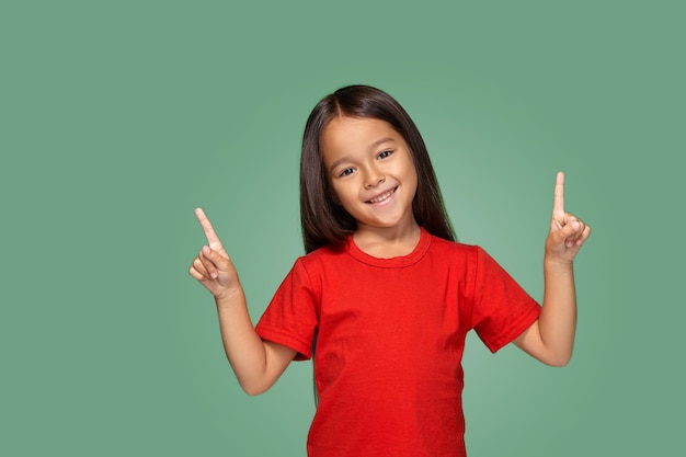 Little girl in red t-shirt with finger up on a green background