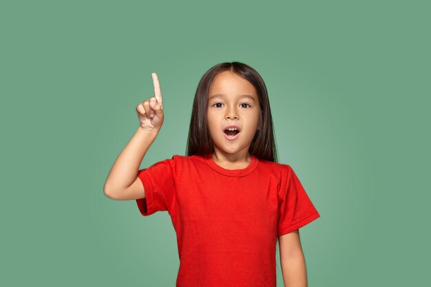 Маленькая девочка в красной футболке с поднятым пальцем на зеленом фоне