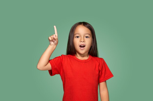 緑の背景に指を上にして赤いTシャツの少女