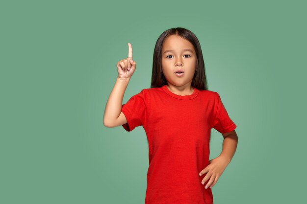 녹색 배경에 손가락을 올려놓은 빨간 티셔츠를 입은 어린 소녀