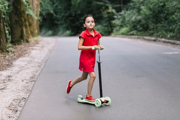 Маленькая девочка верхом нажимает скутер на дороге