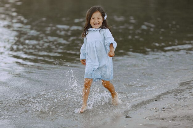 Little girl on the river. Girl splashes water. Girl in a blue dress.