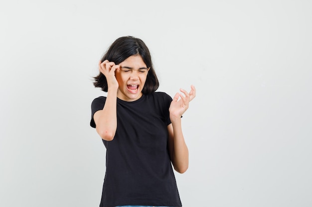 Little girl rubbing temples in black t-shirt and looking forgetful. front view.