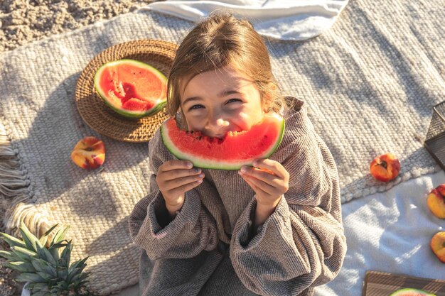 A little girl on a sandy sea beach eats a watermelon