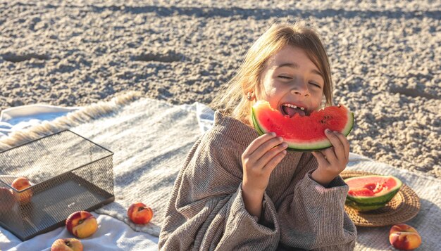 A little girl on a sandy sea beach eats a watermelon