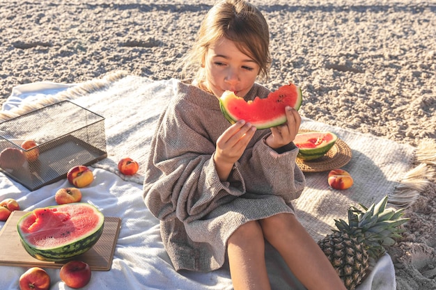 Маленькая девочка на песчаном морском пляже ест арбуз